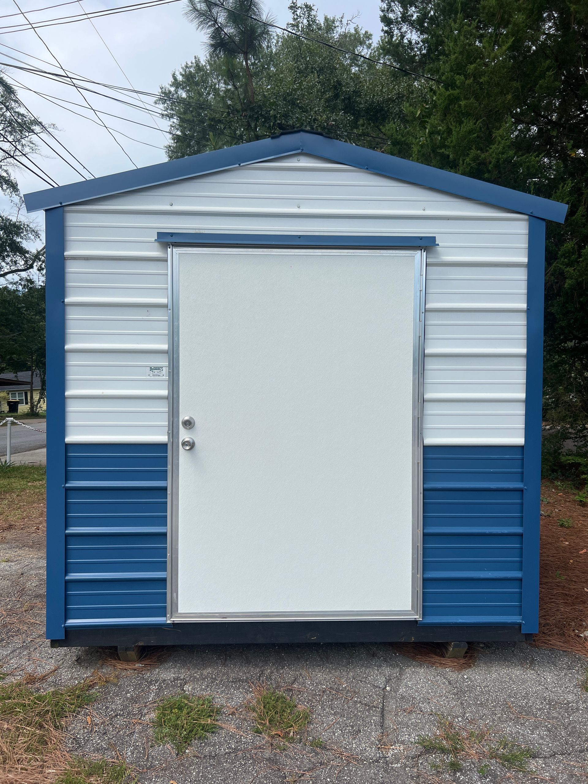 Small white and blue storage shed with a single door on a gravel lot