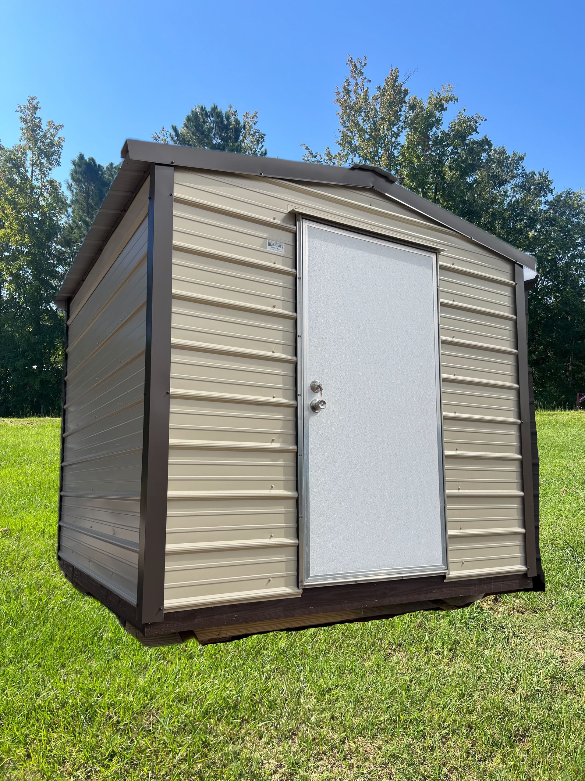 Small beige and brown storage shed with white door on a grassy lawn under a blue sky