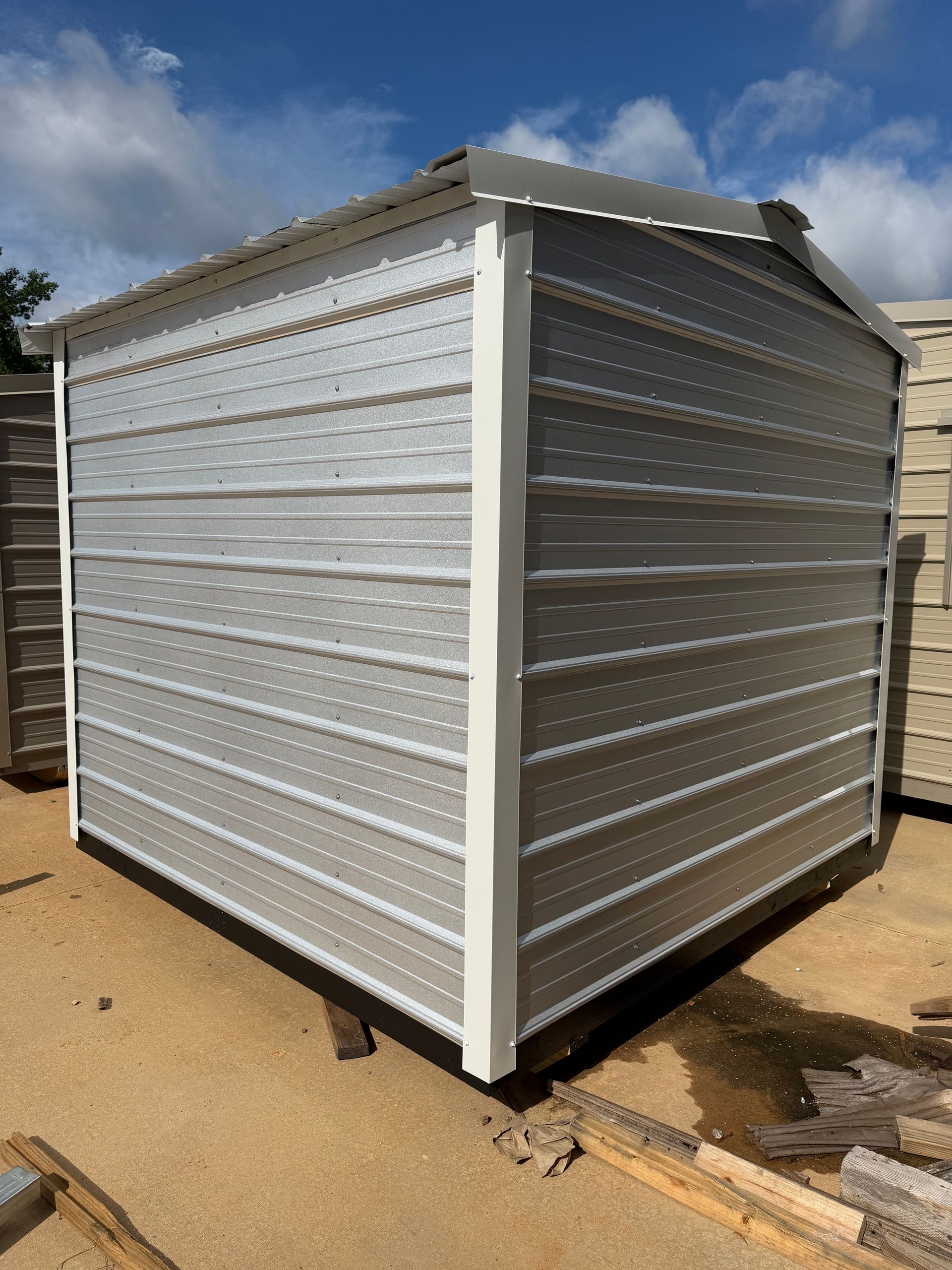 Small gray metal shed with corrugated walls and a sloped roof on a dirt lot under a blue sky