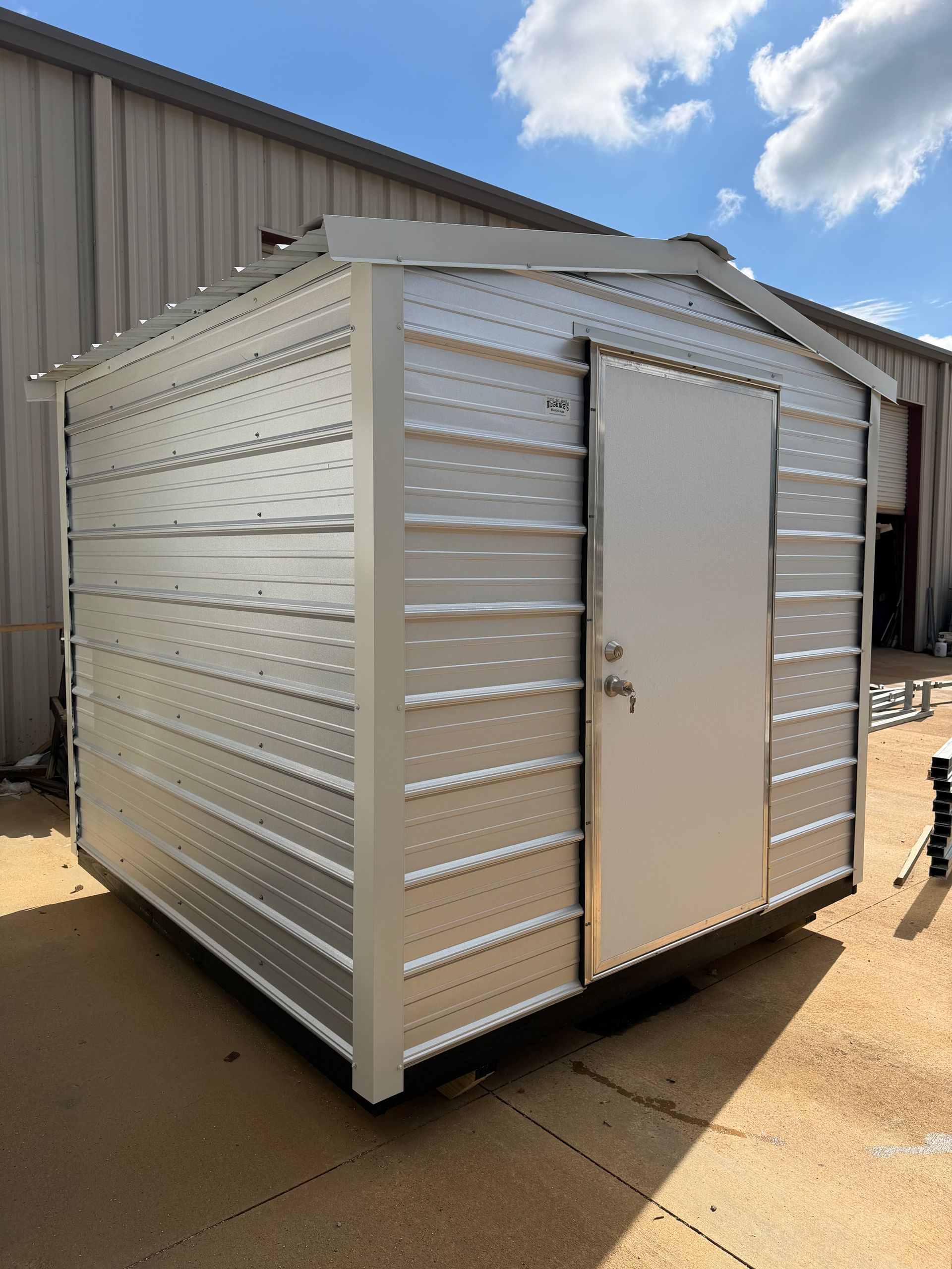 Small metal storage shed with a white door, standing on grass under a blue sky.