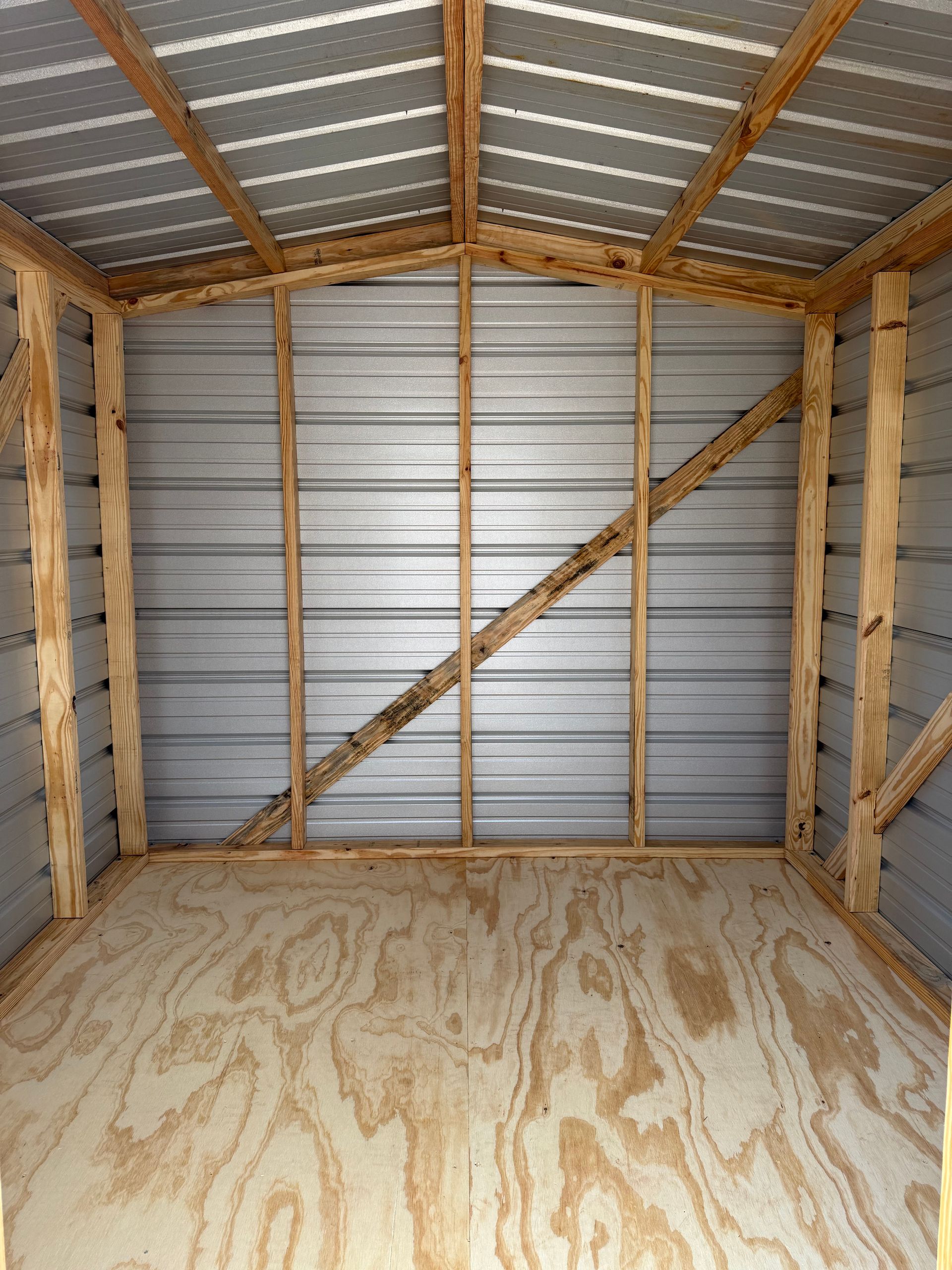 Interior of a small unfinished shed with plywood floor, exposed wood framing, and corrugated metal walls and roof.
