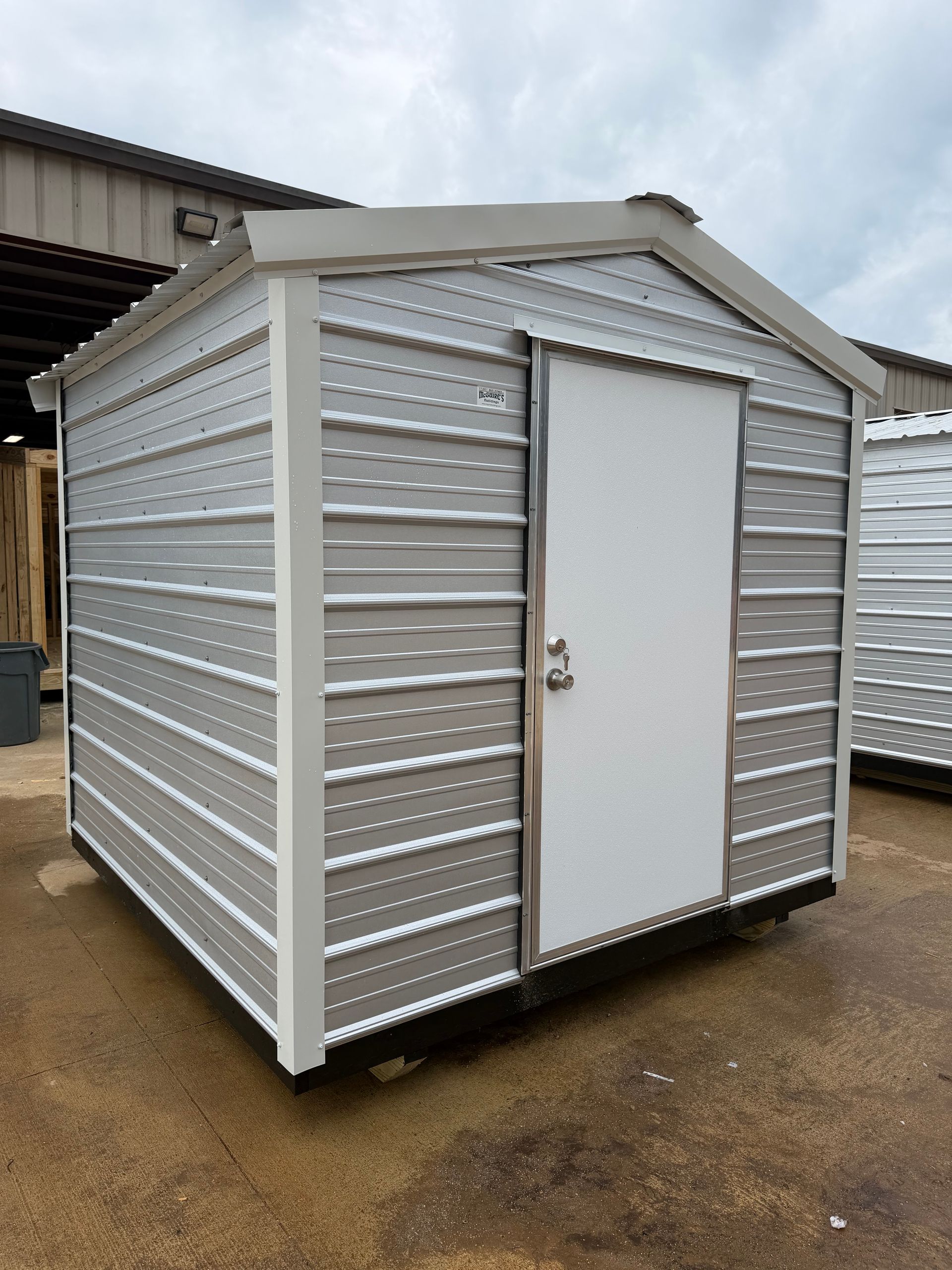 Small silver metal storage shed with a white door on a wet concrete surface.