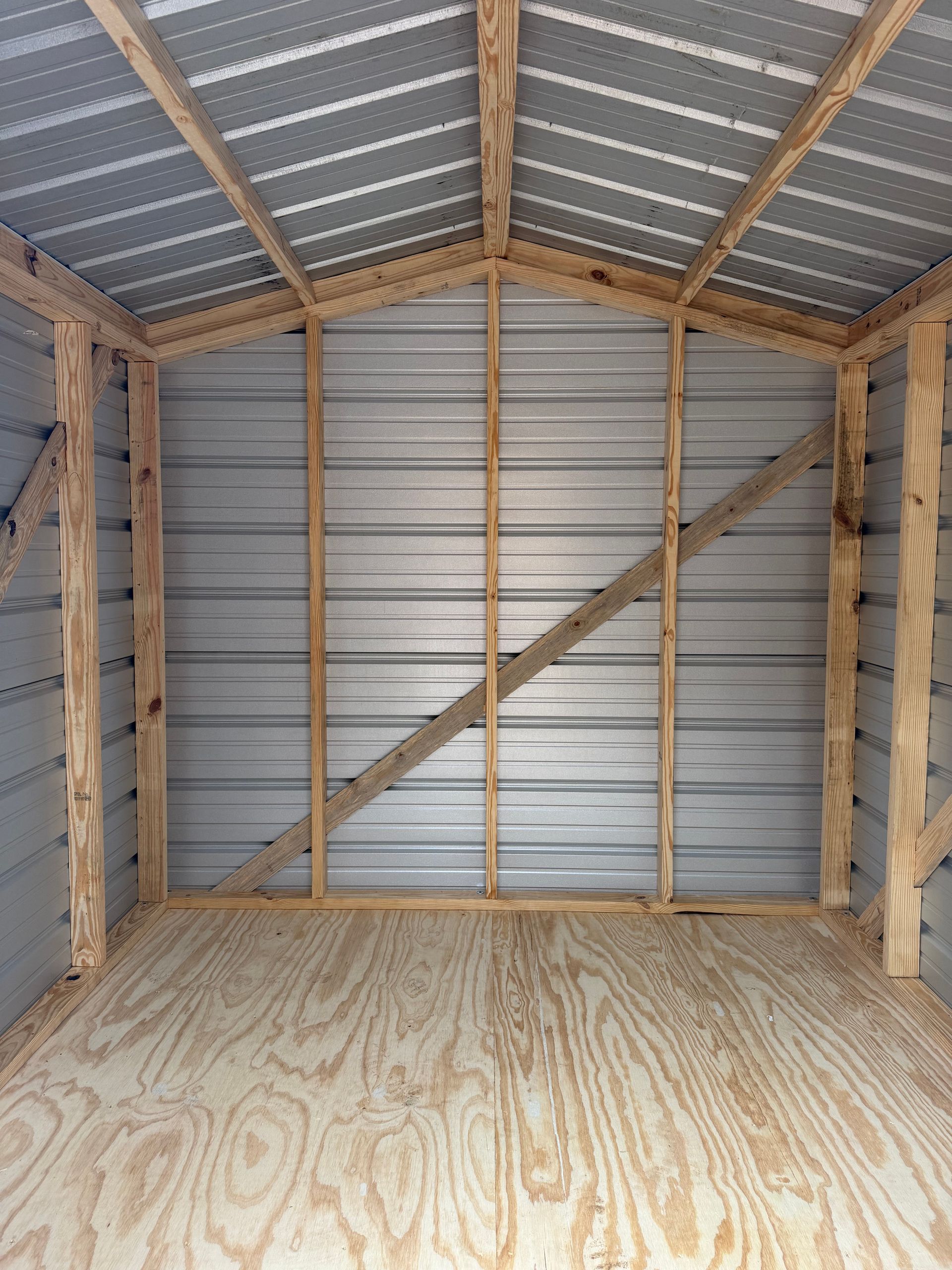 Empty wooden shed interior with plywood floor, corrugated metal walls, and exposed roof framing.