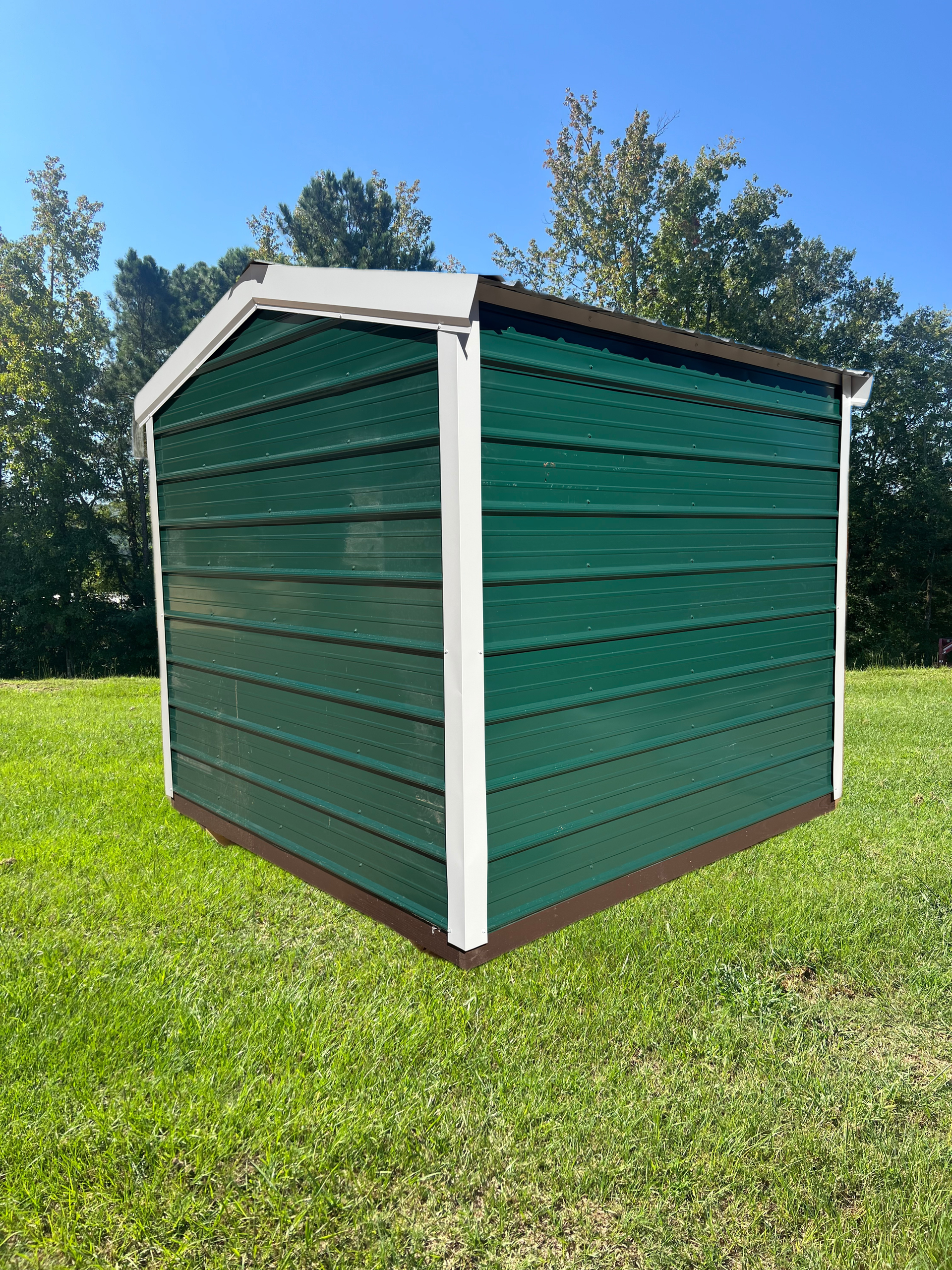 Green wooden shed with white trim sitting on a grassy lawn under a blue sky.