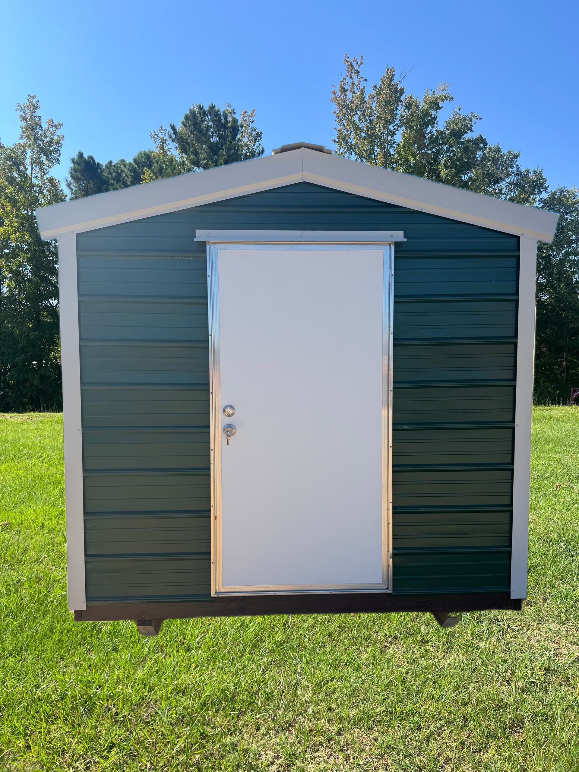 Small green shed with white trim and door, standing on grass under a blue sky.