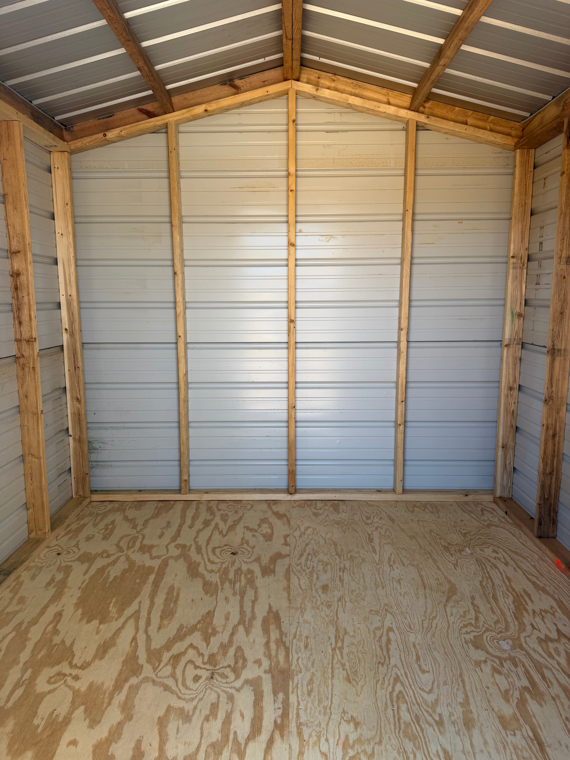 Empty unfinished shed with plywood floor and metal walls under a sloped roof