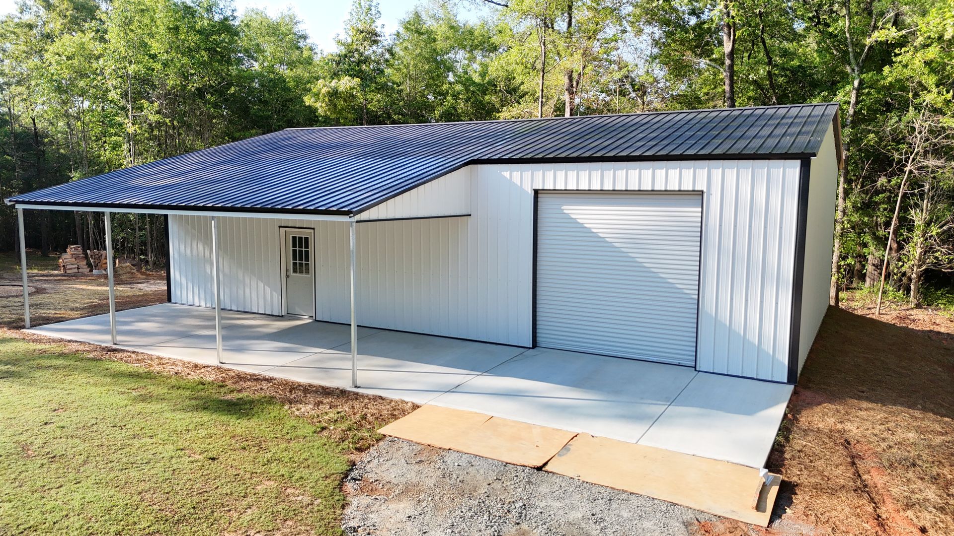 White metal building with a blue corrugated roof, a concrete porch, and a closed garage door.