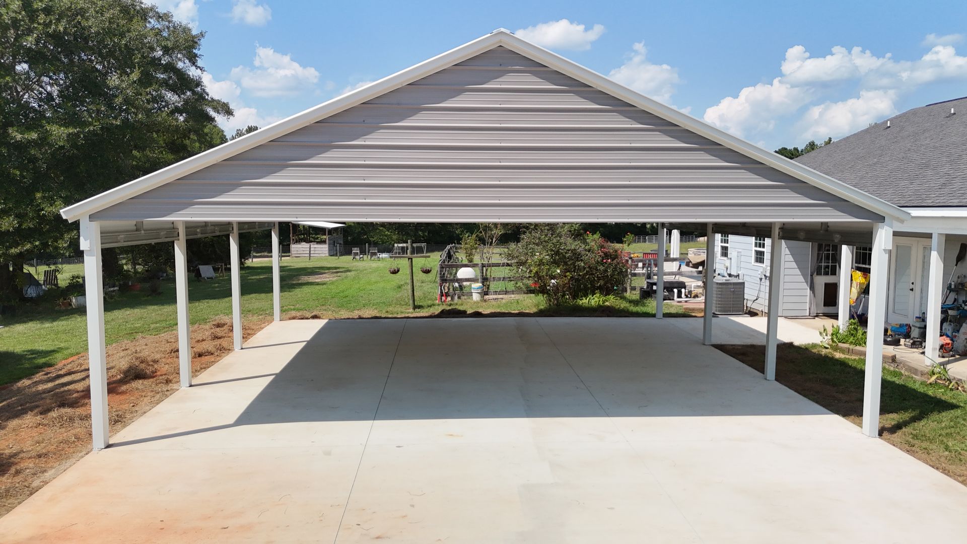 Gray metal carport with white supports over a concrete driveway.