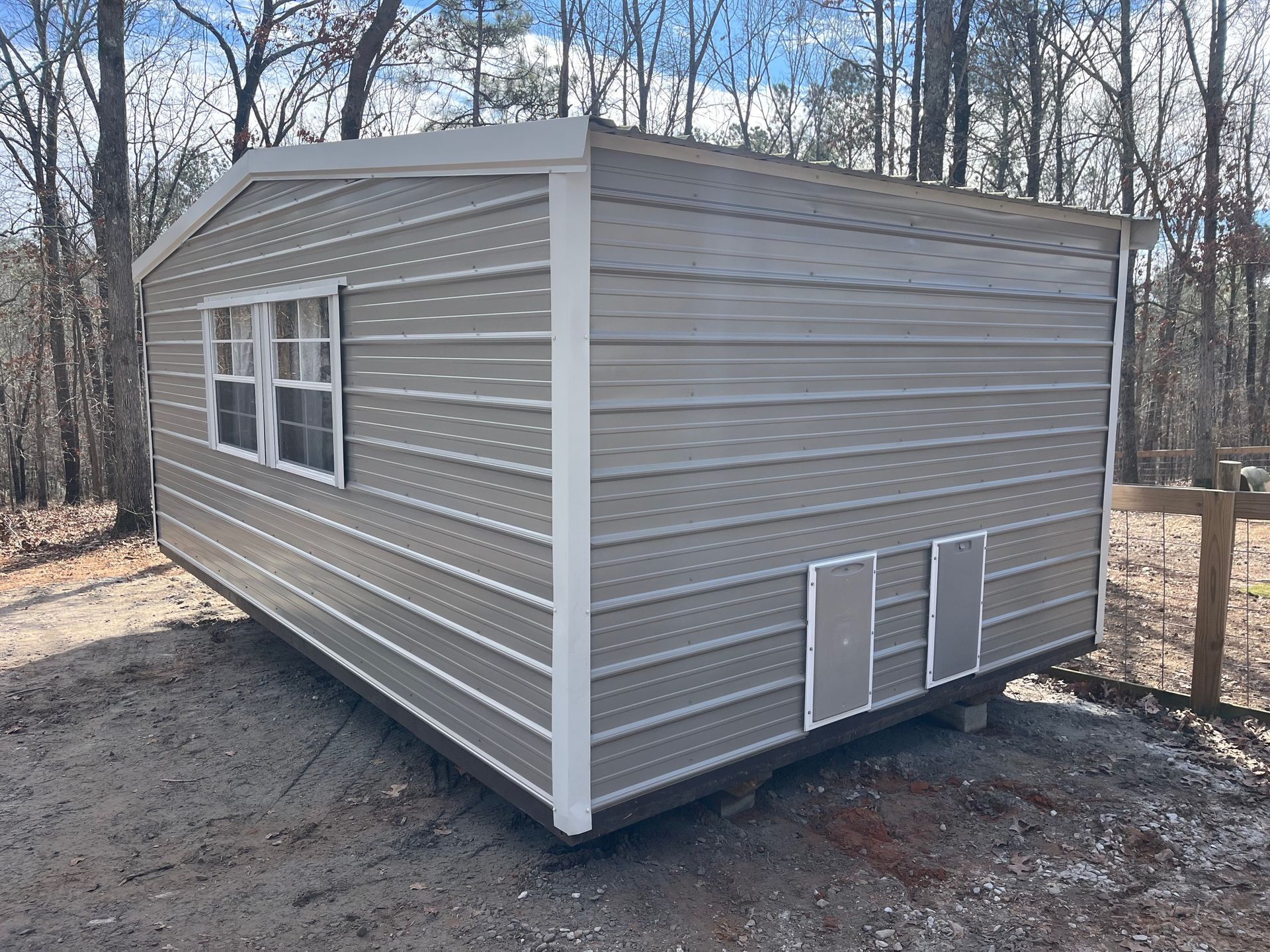 Gray shed with white trim, two windows, and vents, set on gravel, outdoors.