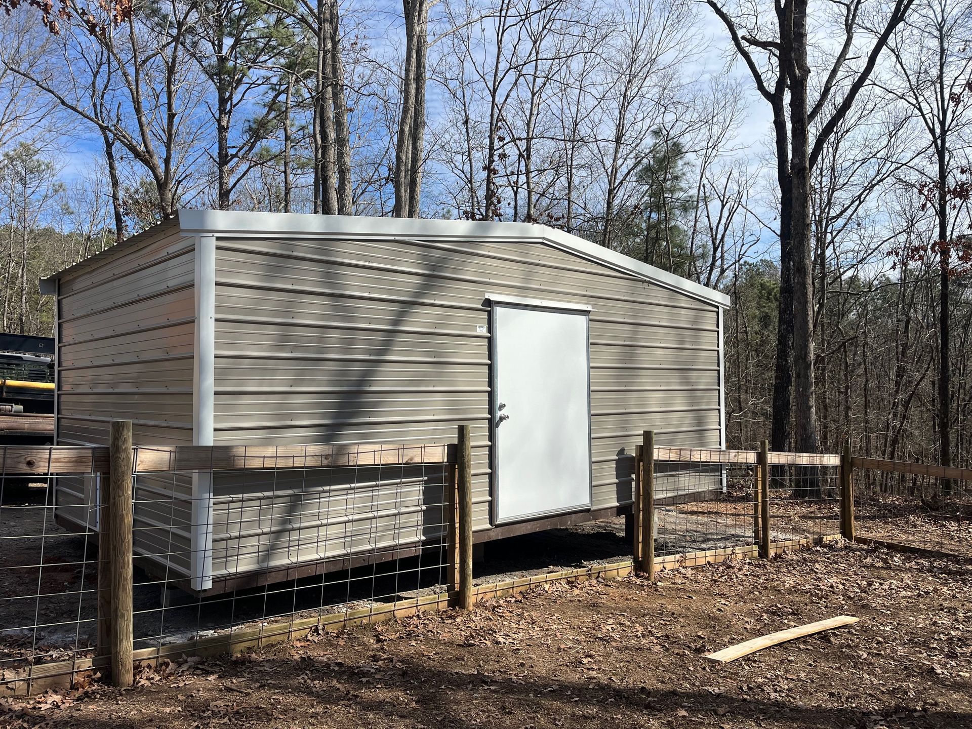Metal shed with a white door, brown siding, and white trim, in a wooded area.