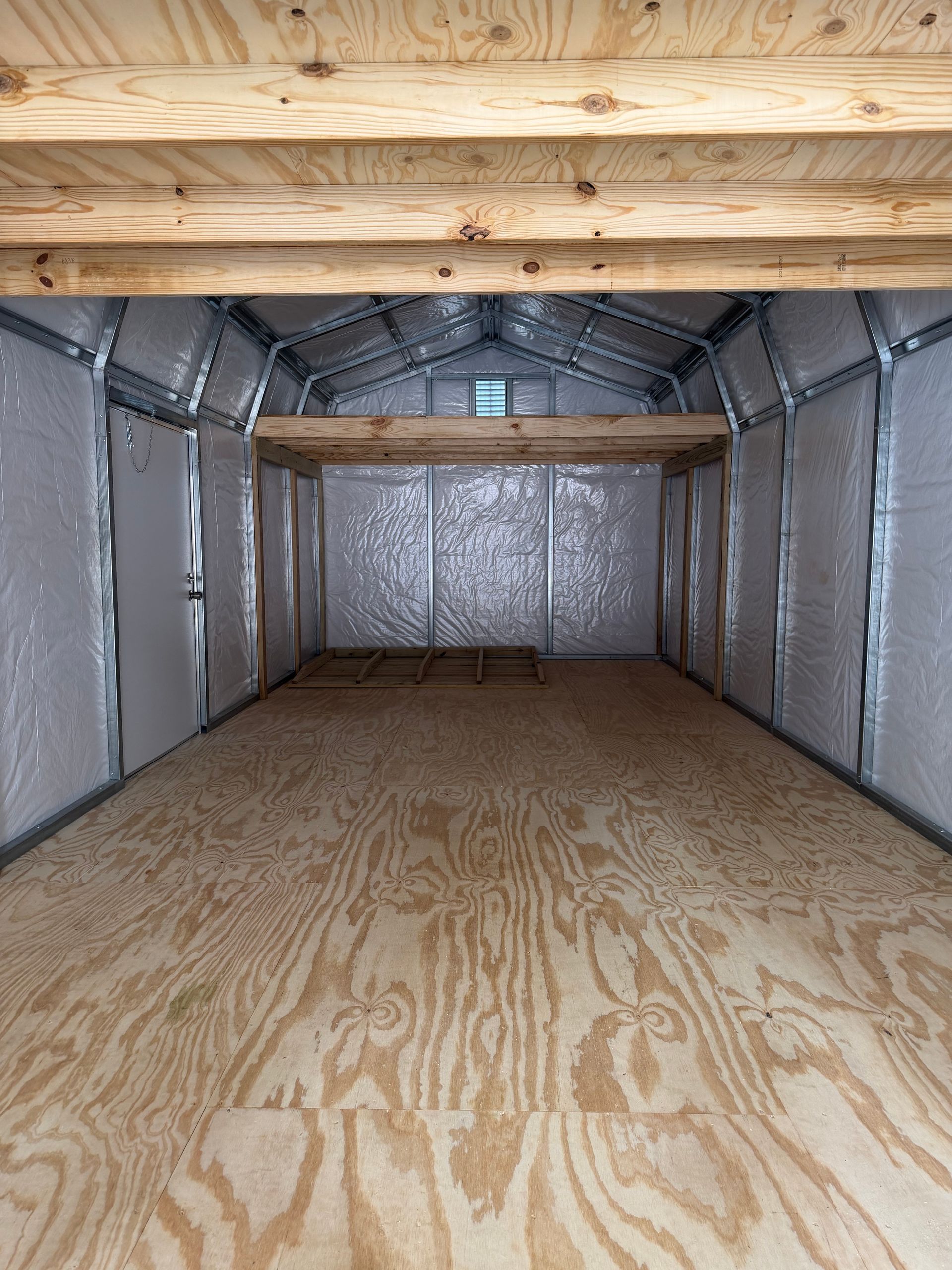 Empty insulated metal storage trailer interior with plywood floor and wooden roof beams