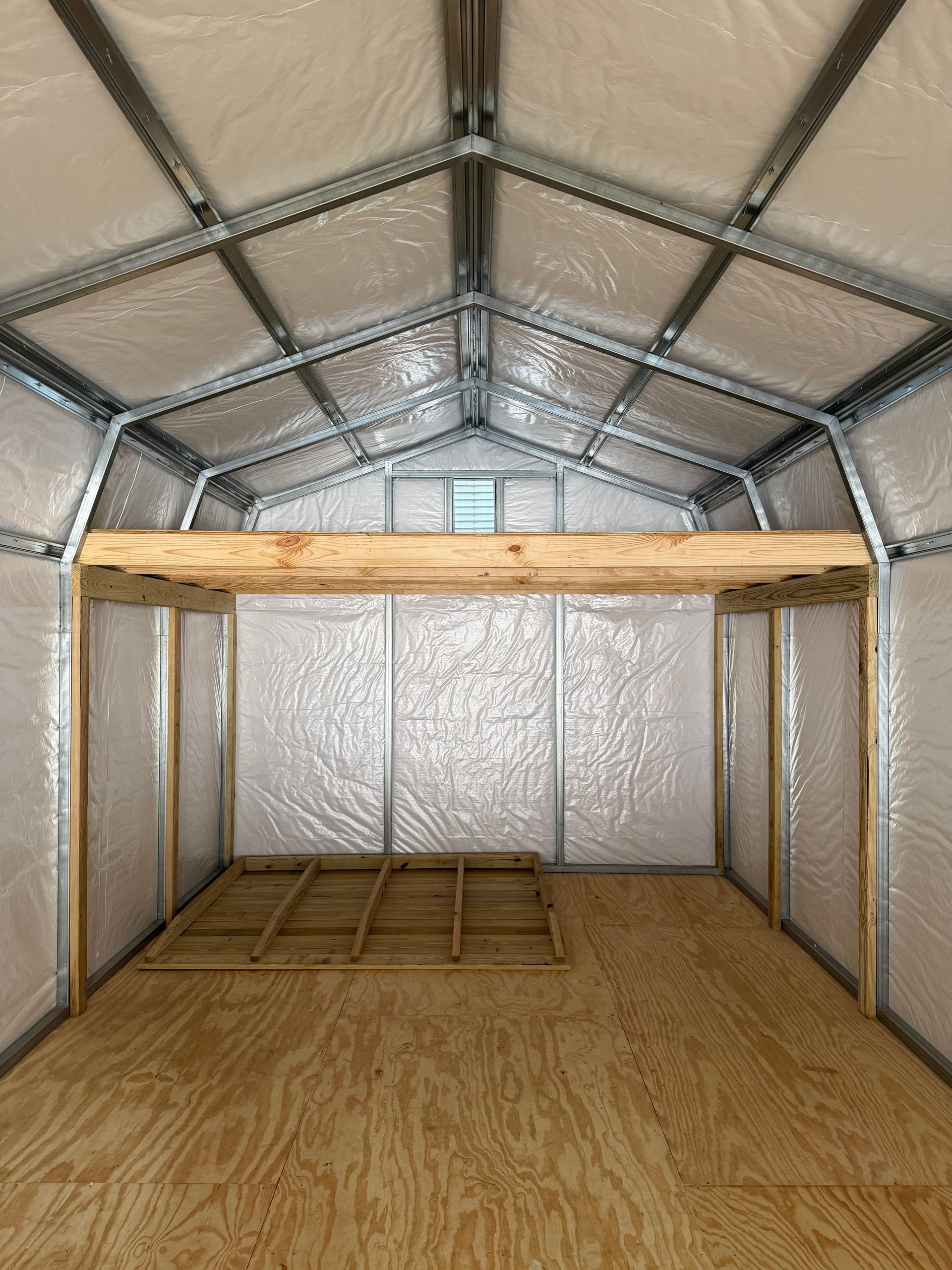Empty shed interior with plywood floor, metal walls, and a wooden loft frame near the back