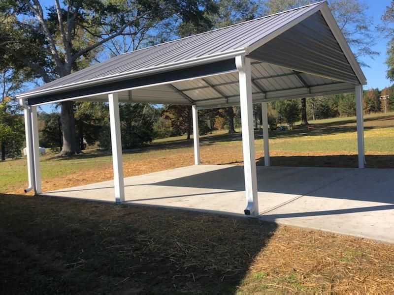Carport with gray metal roof, white supports, on a concrete pad, in a grassy area.