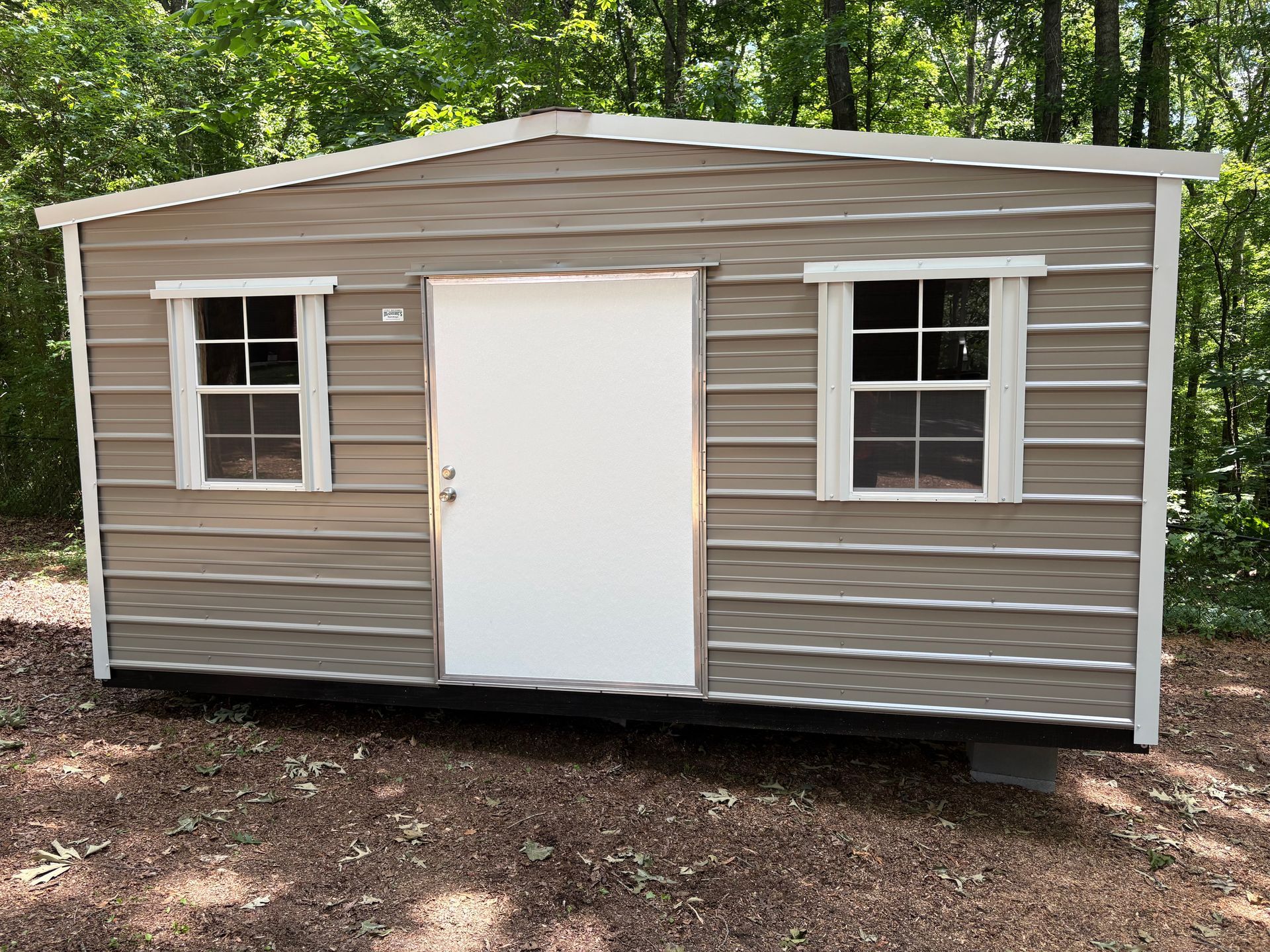 Small beige shed with white door and windows in a wooded yard