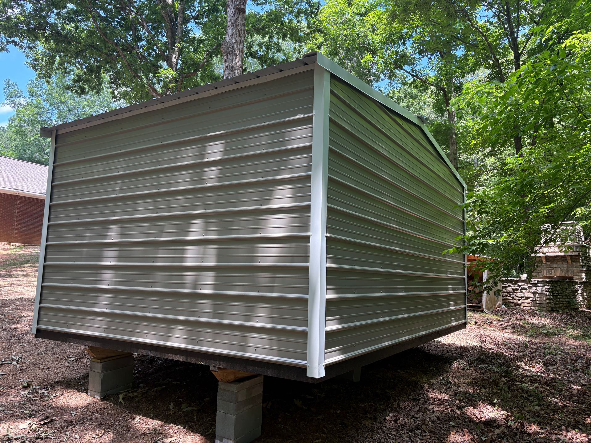 Small silver-sided shed raised on cinder blocks in a wooded yard