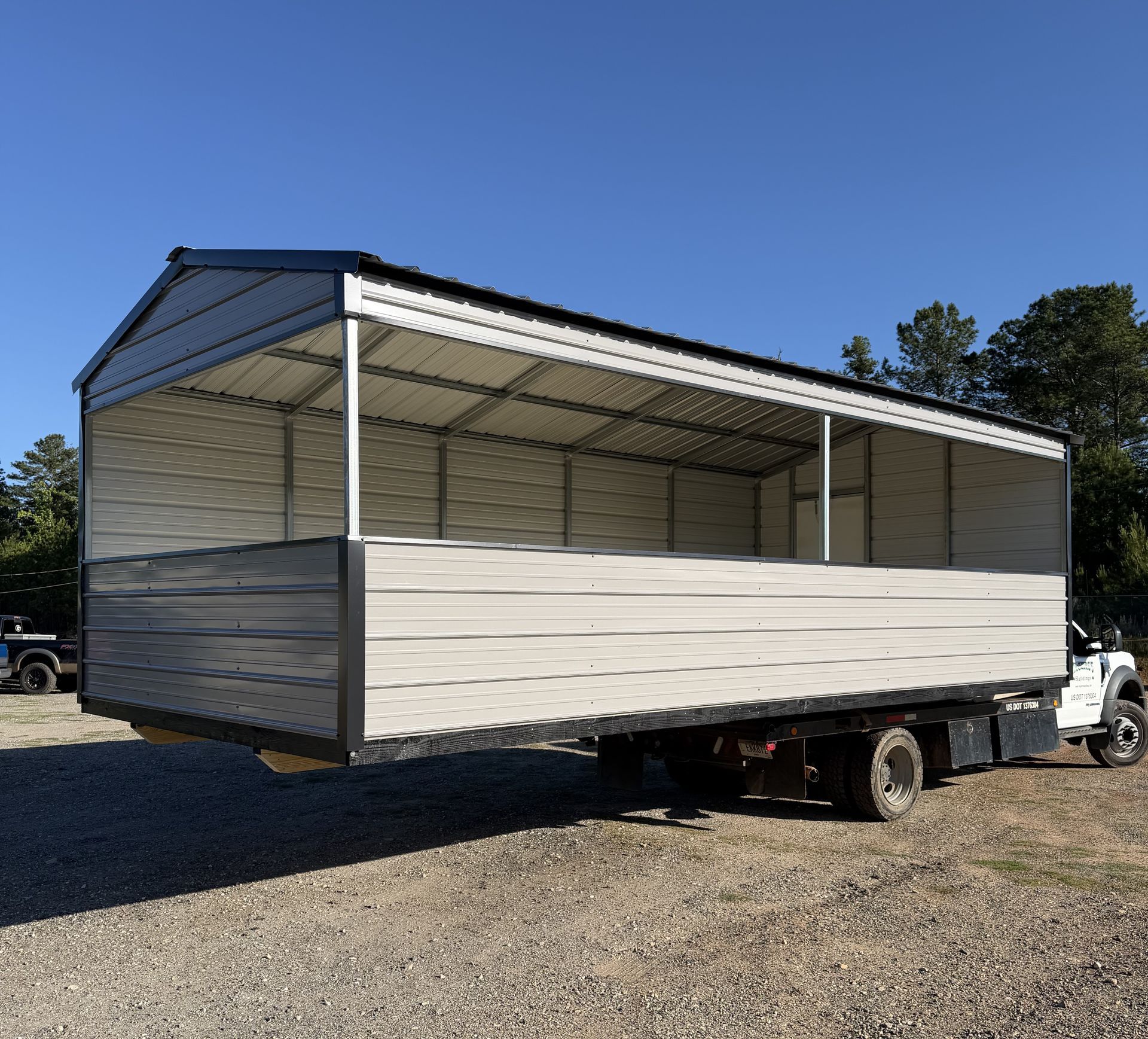 White utility trailer with open sides and blue roof parked on gravel under a clear sky.