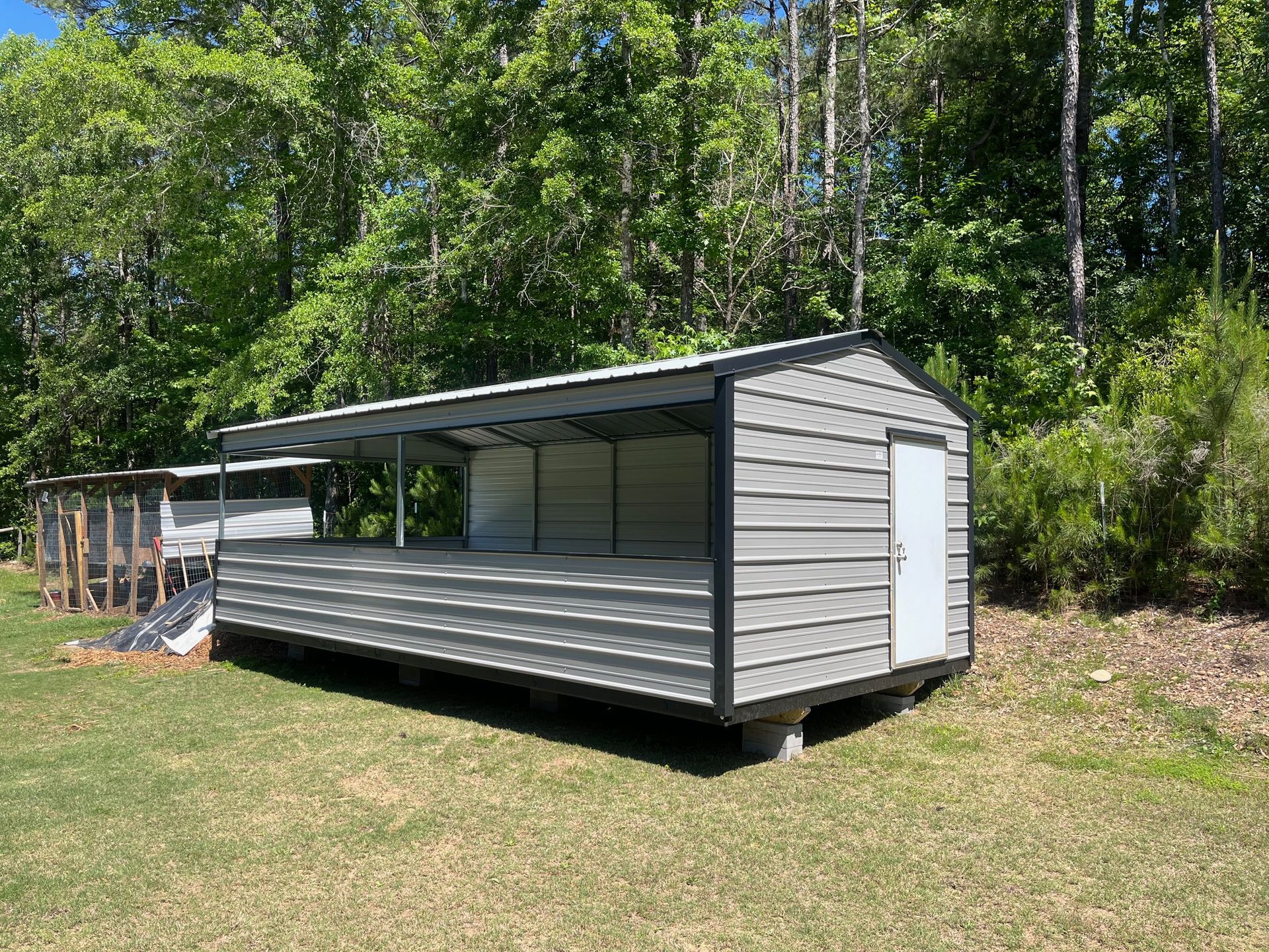 Small gray shed with a slanted roof beside a wooded area and grassy yard