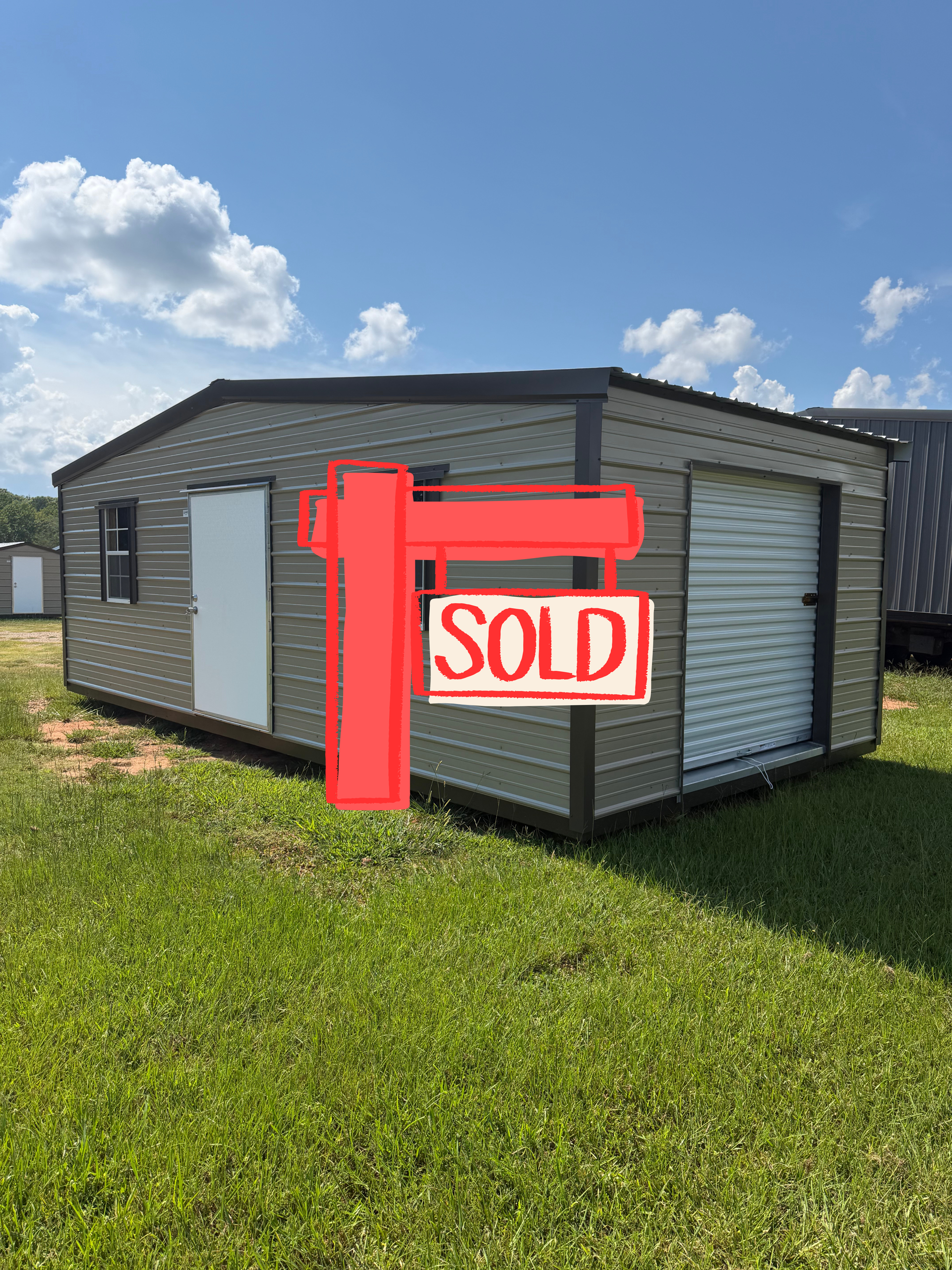 Gray manufactured home with a red “SOLD” sign in a grassy lot under a blue sky
