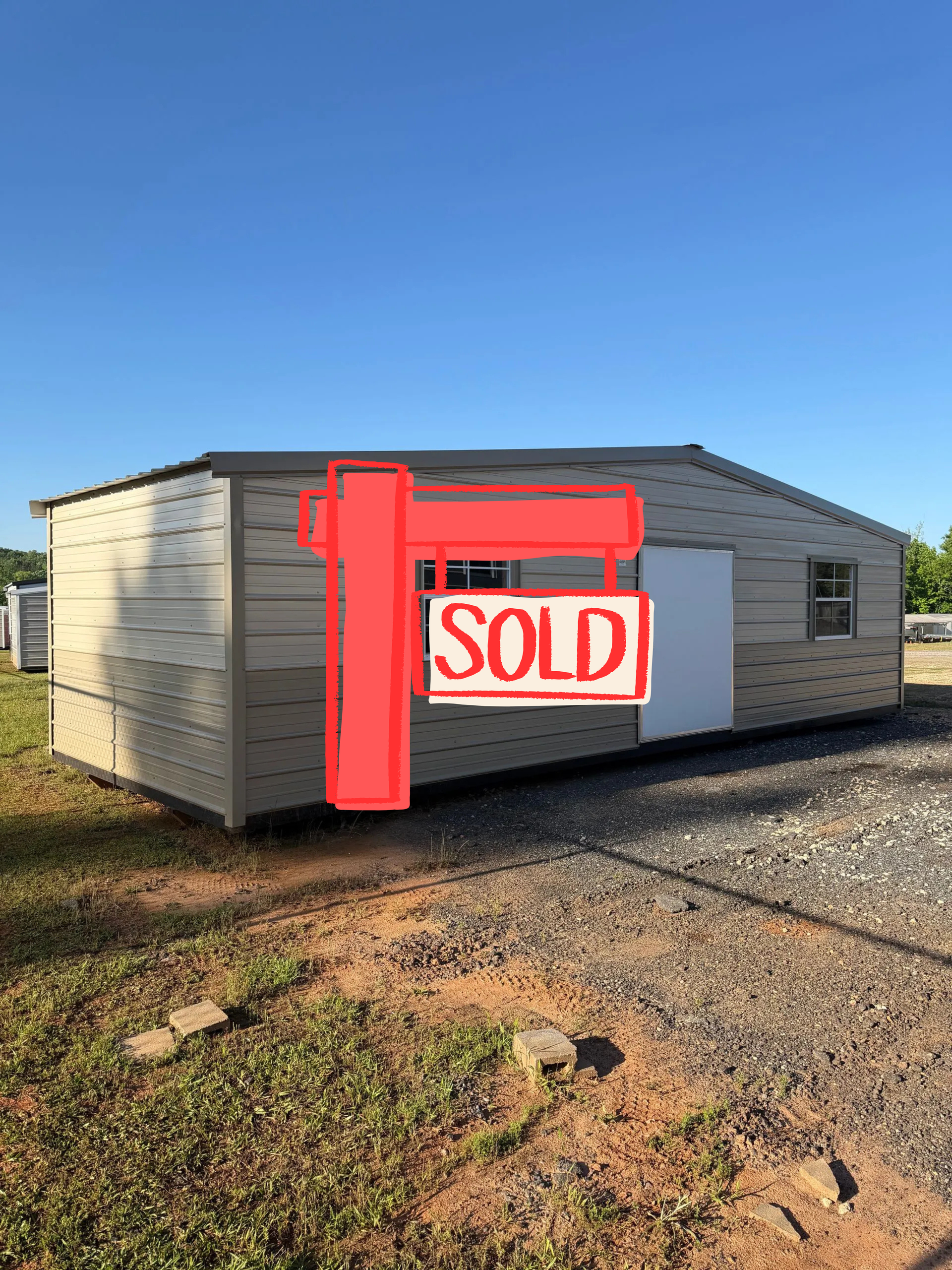 Small beige utility building with white door and windows on gravel under a clear blue sky