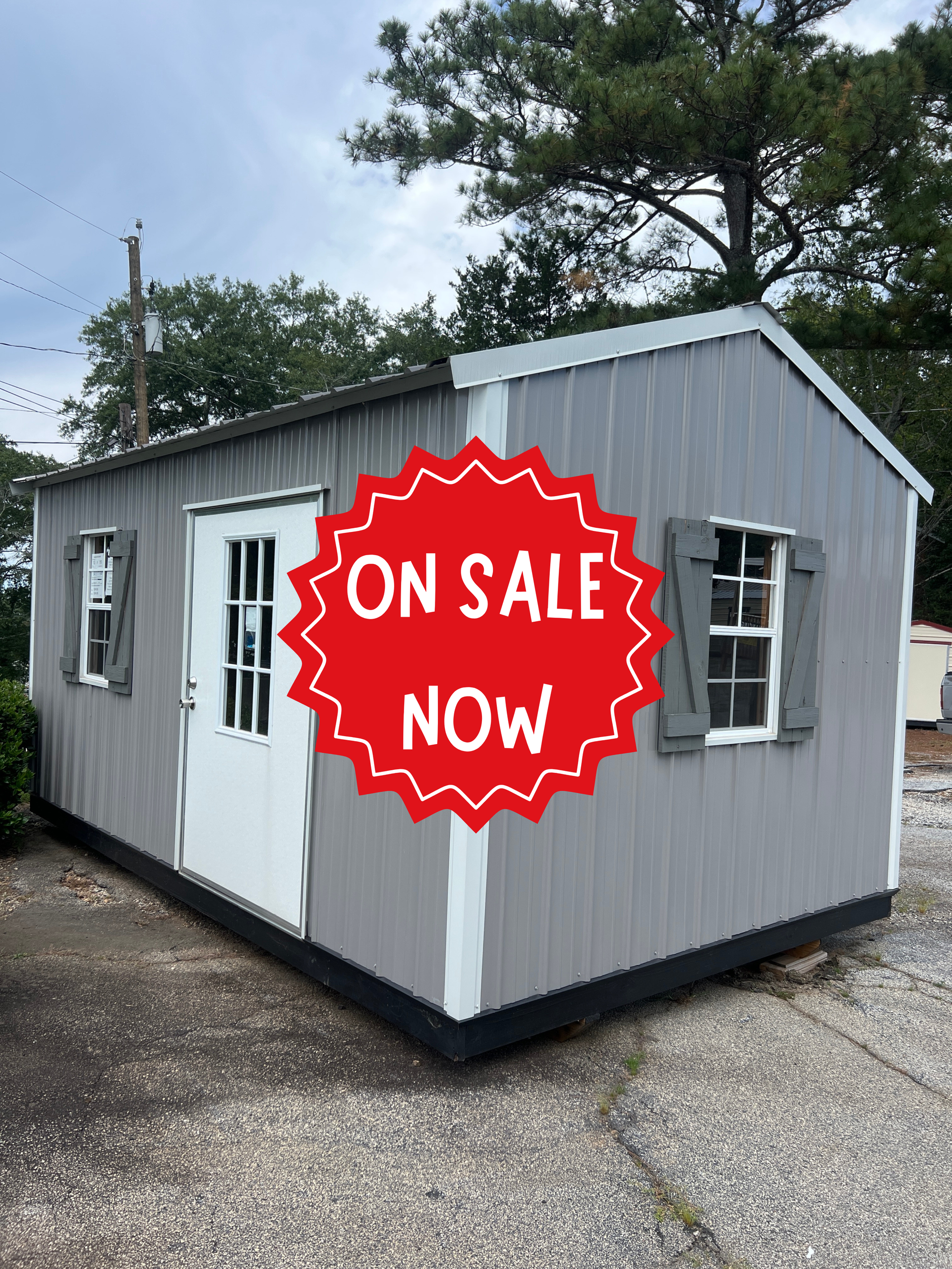 Gray portable building with a red “On Sale Now” sign on the side outdoors