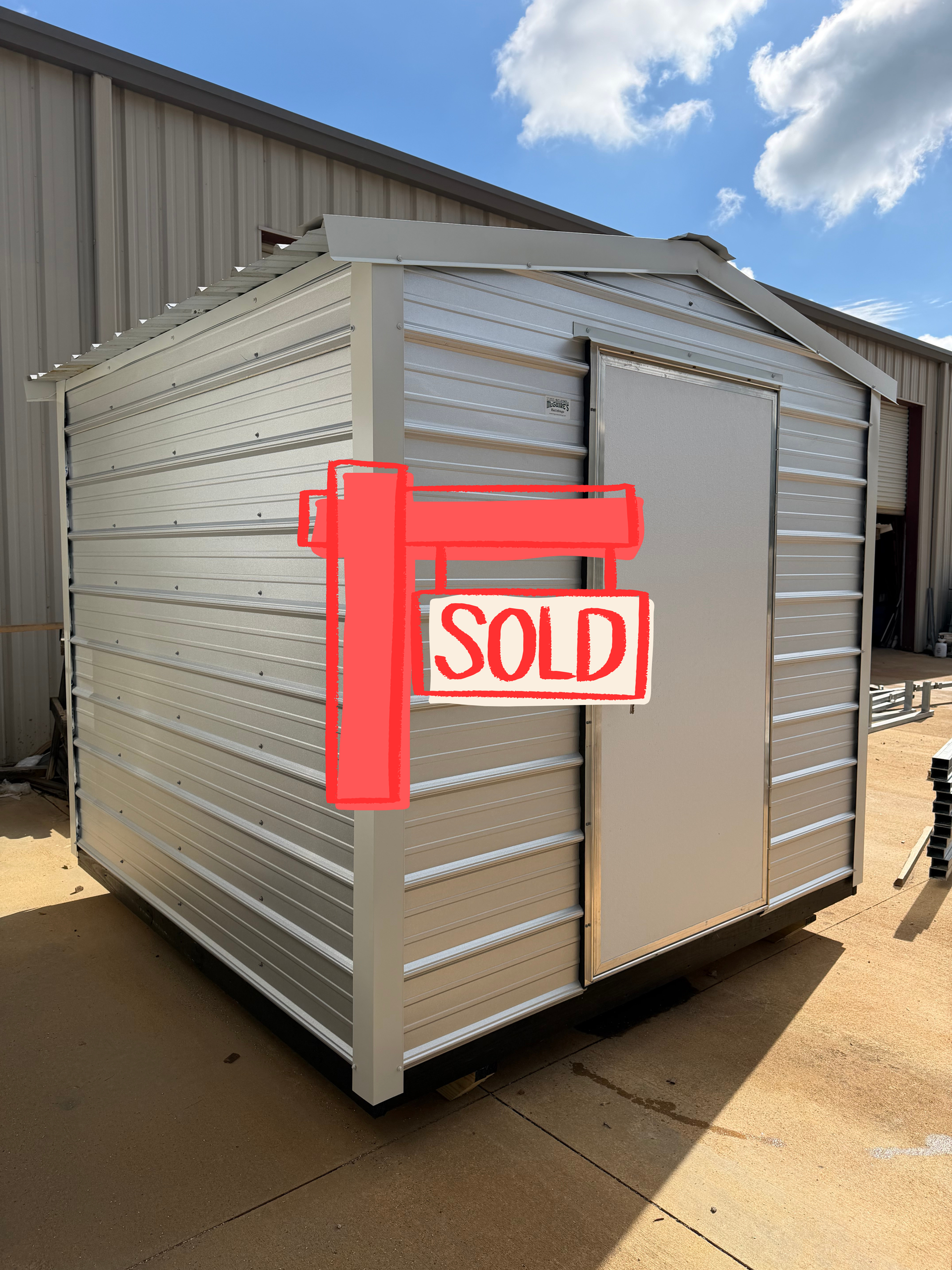 Silver metal storage shed with red SOLD sign on the side outdoors