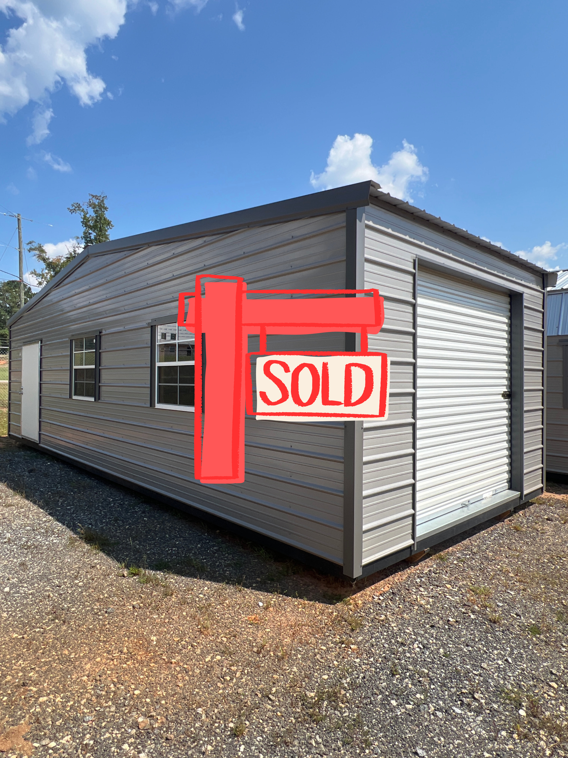 Gray modular building with a red “SOLD” sign on the front, viewed from the corner outdoors.