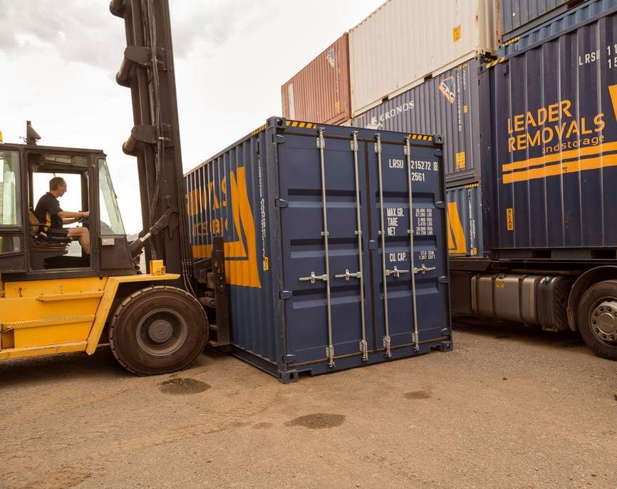 A Forklift is Loading a Blue Shipping Container Into a Truck — Leader Removals & Storage in Goulburn, NSW