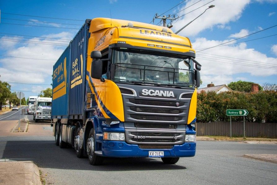 A Blue and Yellow Scania Truck is Driving Down a Street — Leader Removals & Storage in Mitchell, ACT