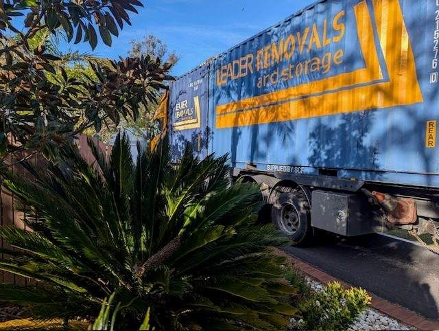 A Large Blue Truck is Parked in a Driveway Next to a Palm Tree — Leader Removals & Storage in Bowral, NSW