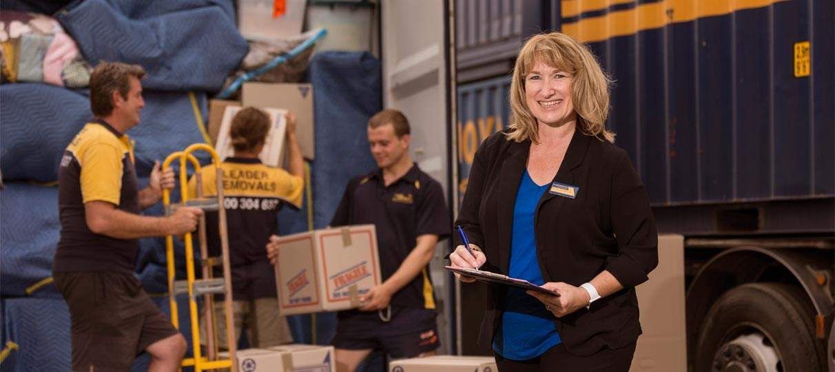 A Woman Is Standing in Front of A Truck Holding a Clipboard — Leader Removals & Storage in Sunshine Coast, QLD