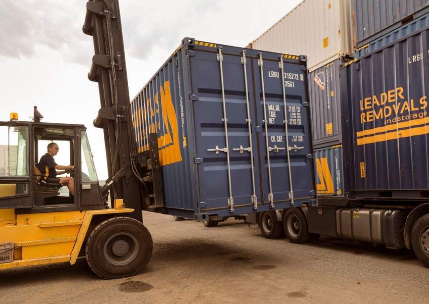A Man is Driving a Forklift Next to a Truck That Says Leader Removals — Leader Removals & Storage in Gold Coast, QLD