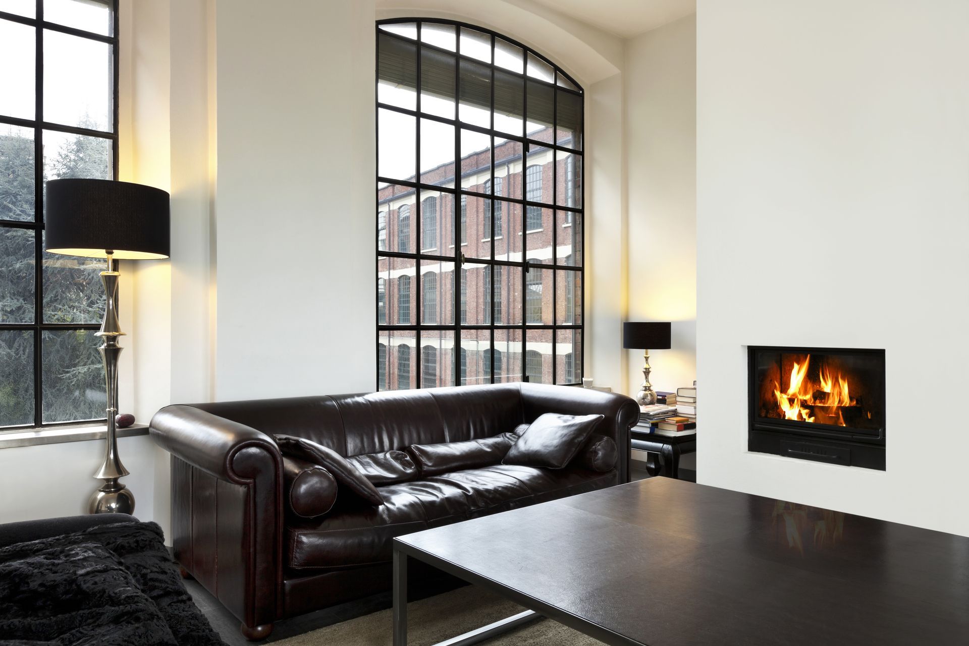 Living room with leather sofa, fireplace, and large windows with a view of a brick building.