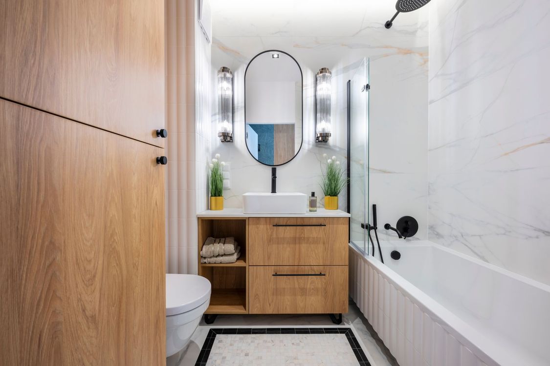 Modern bathroom with wooden vanity, oval mirror, and white marble tiles.