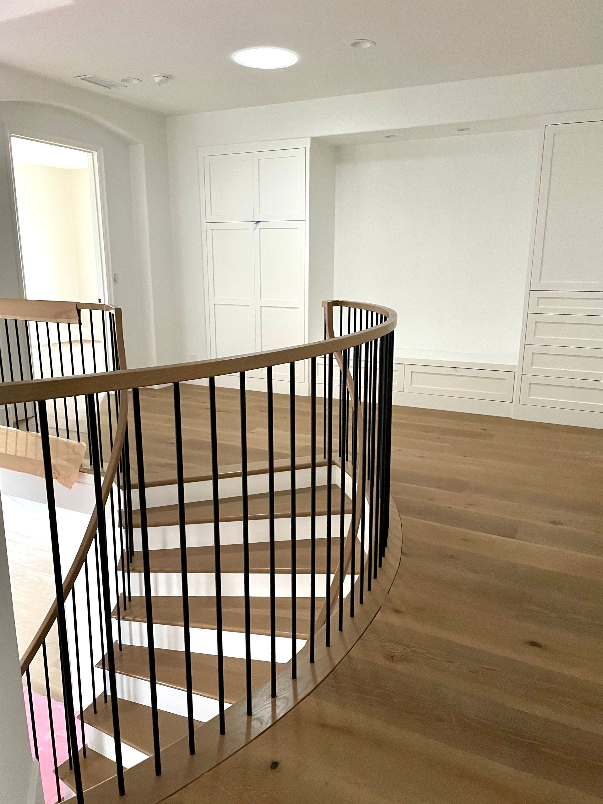 Wooden staircase with black railings, leading up to a landing with light wood flooring. White walls, round skylight.