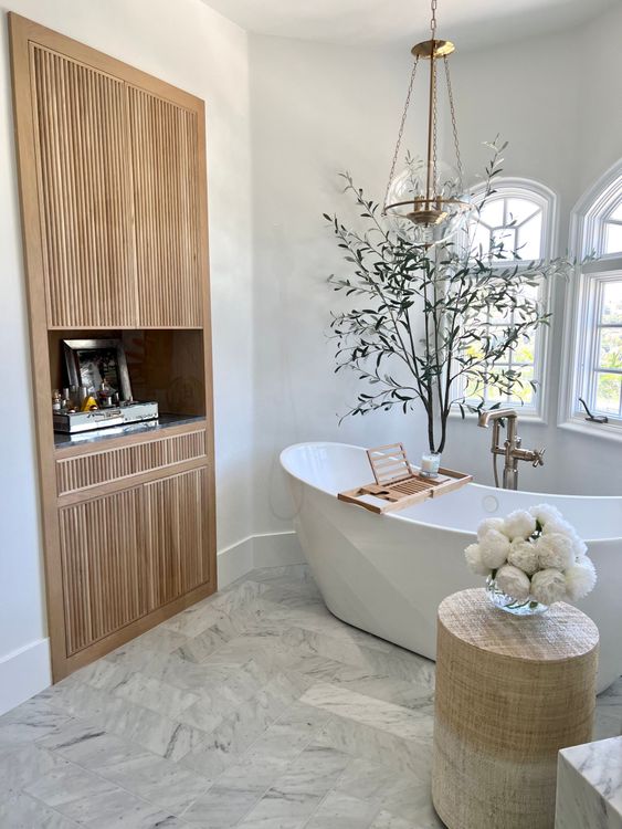Luxurious bathroom with a white tub, wooden storage, and a decorative floral arrangement.