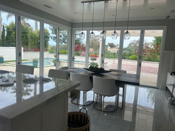 Dining room with table and chairs, glass doors open to a pool and garden.