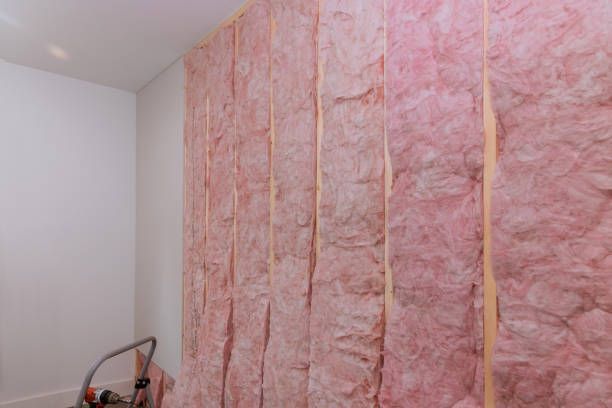 A wall is being insulated with pink fiberglass insulation.