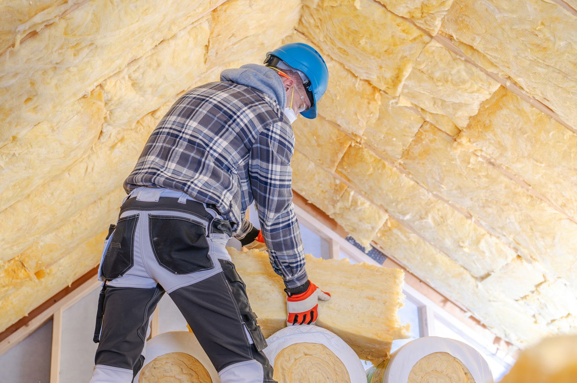 Construction worker installing insulation in residential attic.