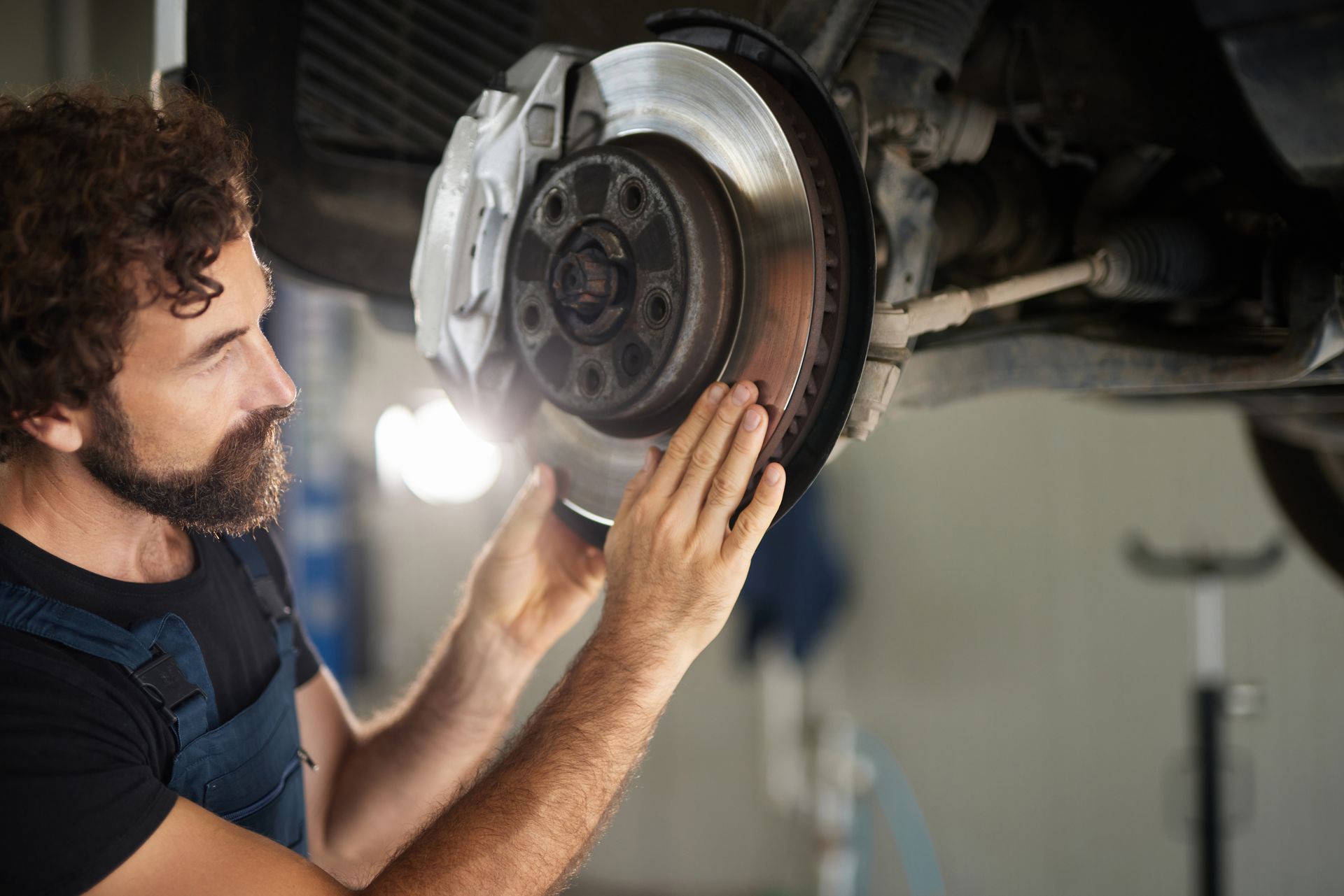 A car mechanic focuses on inspecting and repairing the brake system of a vehicle in a garage space. A car mechanic focuses on inspecting and repairing the brake system of a vehicle in a garage space.