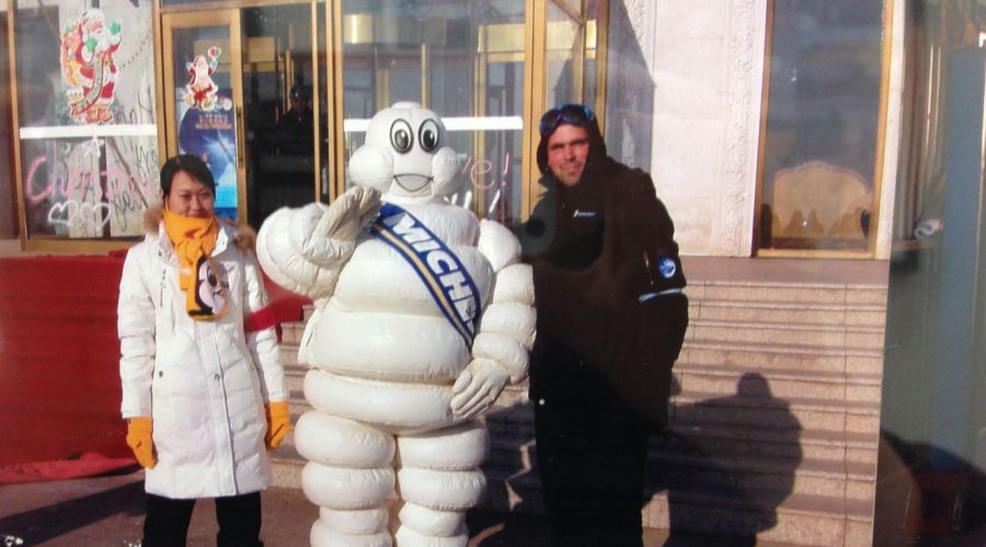 Two people pose with the Michelin Man outside a building with gold accents.