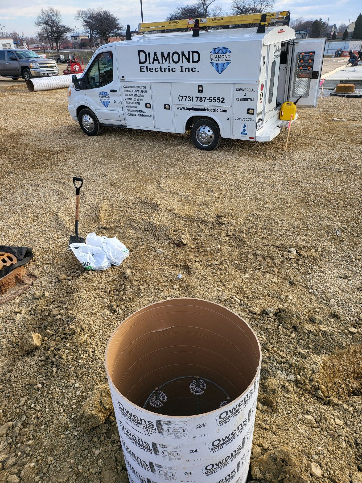 A white van is parked in a gravel lot next to a cardboard bucket.
