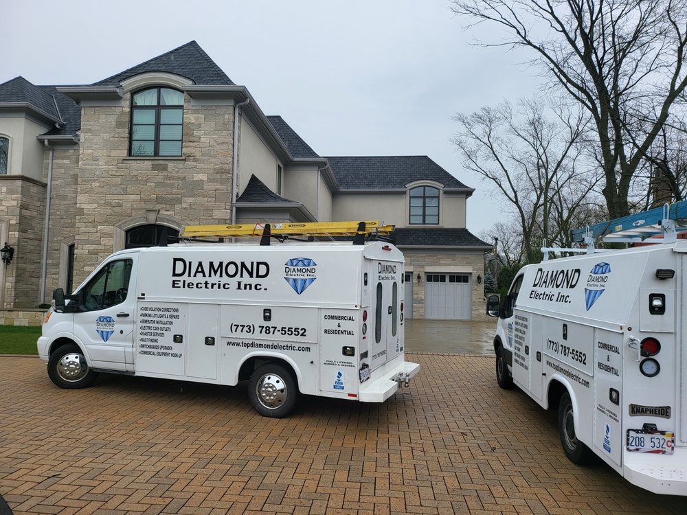 Two diamond electric inc. vans are parked in front of a large house.