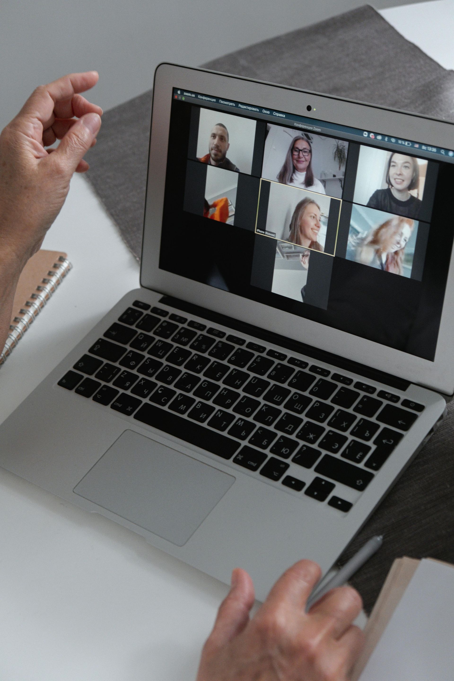 Handen typen op een laptop tijdens een videoconferentiegesprek waarbij meerdere deelnemers op het scherm worden weergegeven.