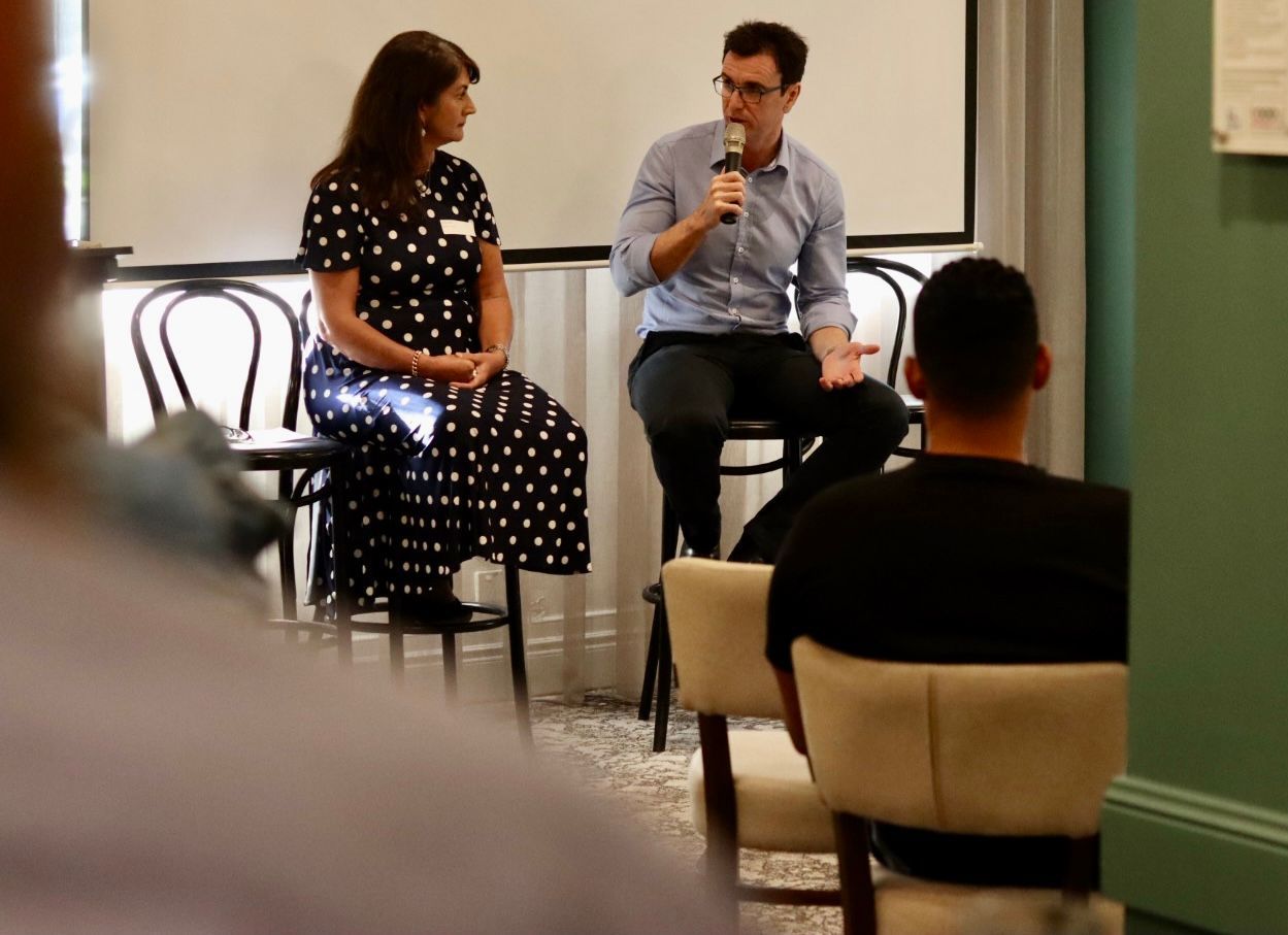 a man is speaking into a microphone while a woman sits behind him