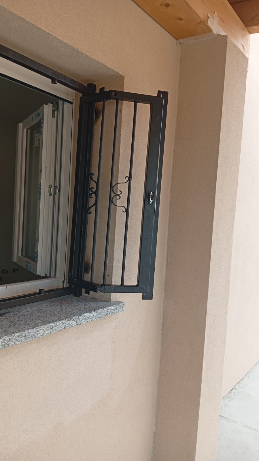 Cancello di sicurezza in metallo nero incernierato a un edificio beige accanto a una finestra con davanzale in pietra.