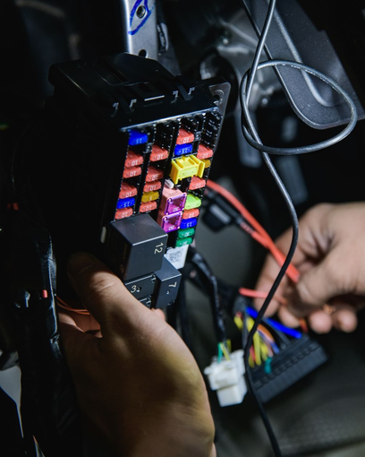 Hands working inside an open car computer case with colorful circuit boards and cables. | Good Deals on Wheels Shop