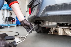 Mechanic using a wrench under a car while the vehicle is lifted in a garage | Good Deals on Wheels Shop