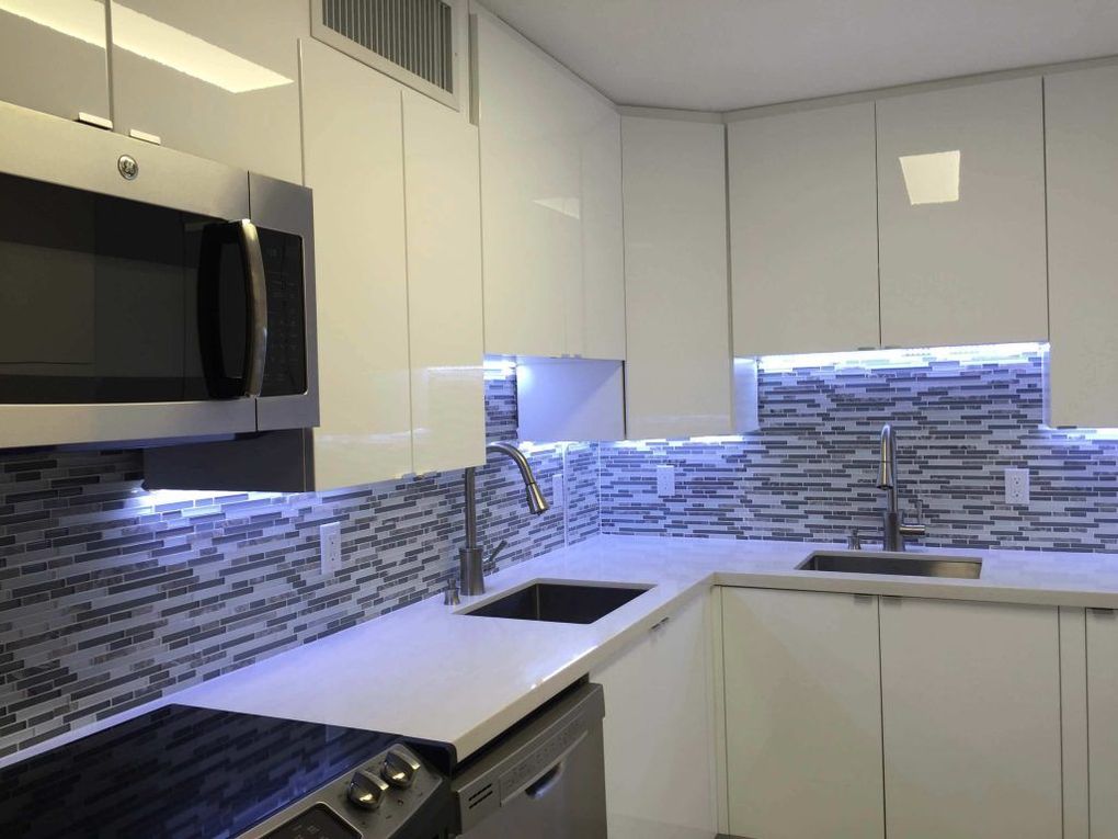 Modern white kitchen with stainless microwave, mosaic tile backsplash, and black countertop sink.