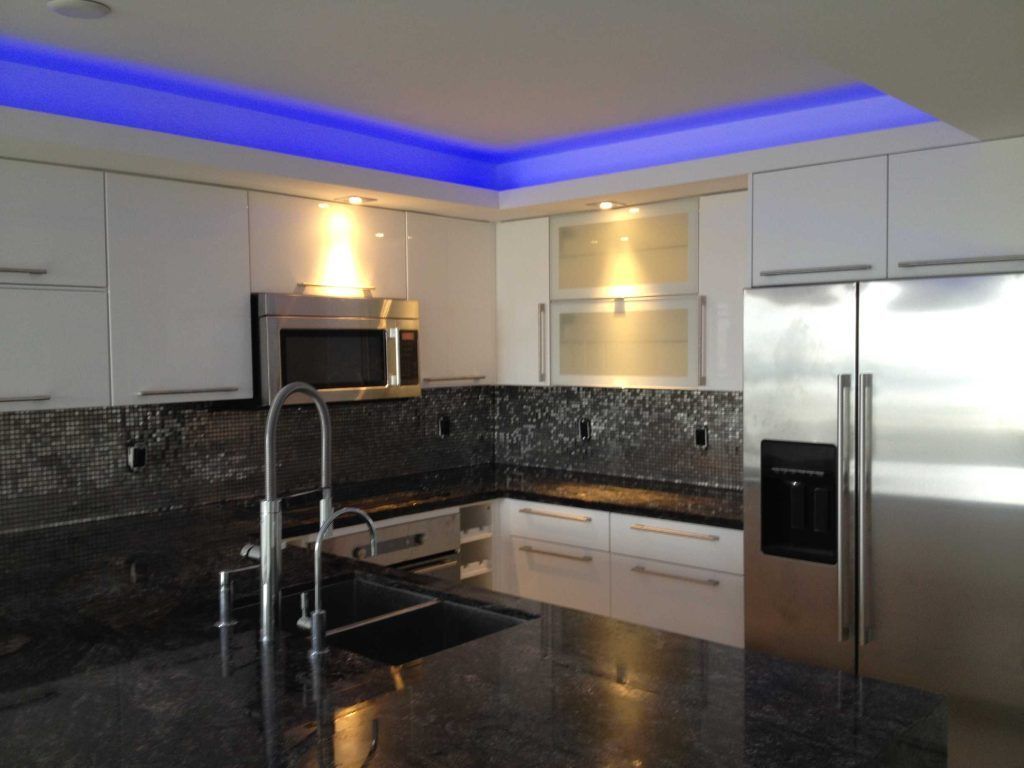 Modern kitchen with white cabinets, black countertops, stainless steel appliances, and blue cove lighting