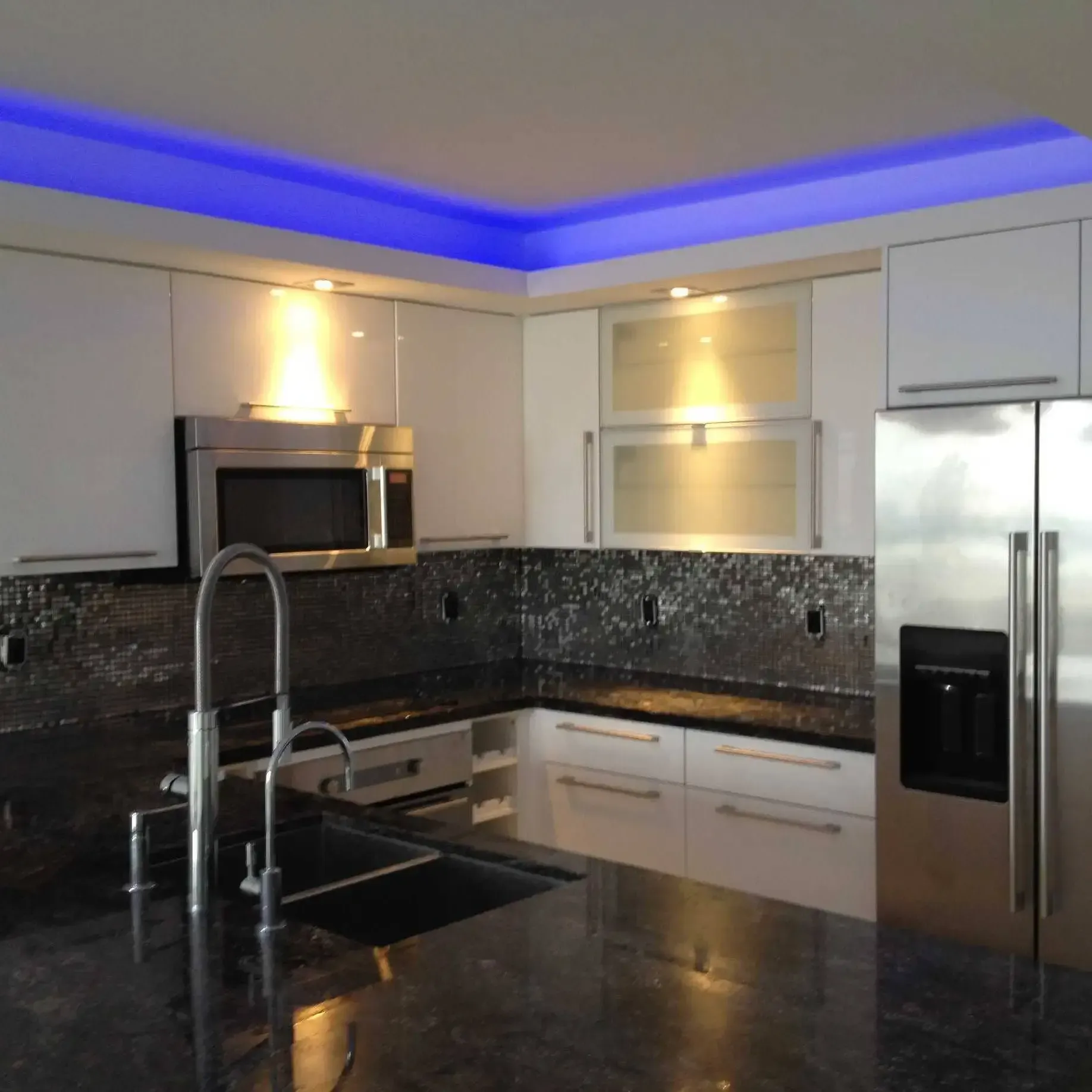 Modern kitchen with white cabinets, black granite counters, stainless appliances, and blue LED ceiling lighting